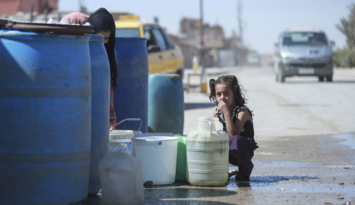 A girl kneeling down with a plastic water container in a road.