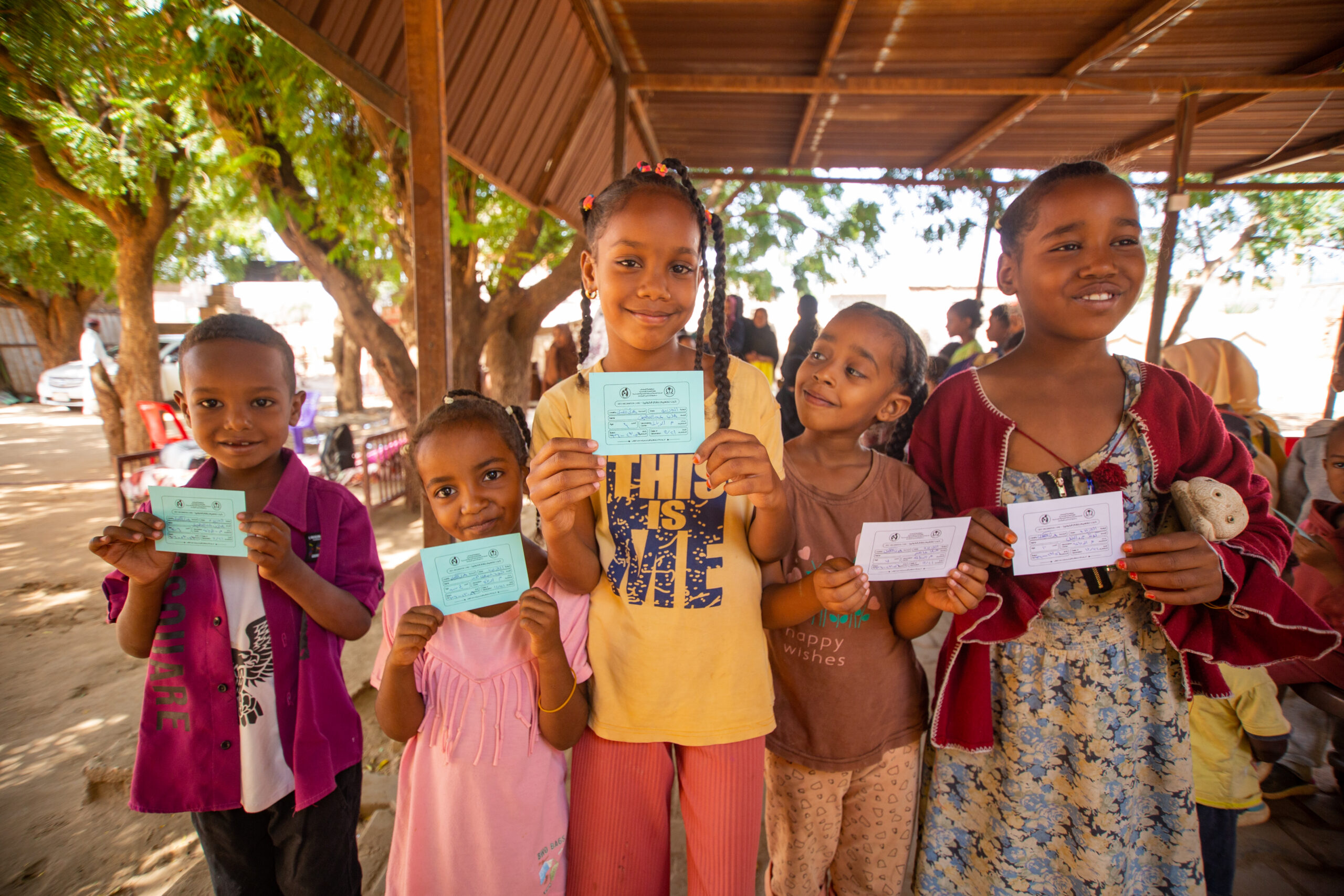 Children standing in a line showing their vaccination cards