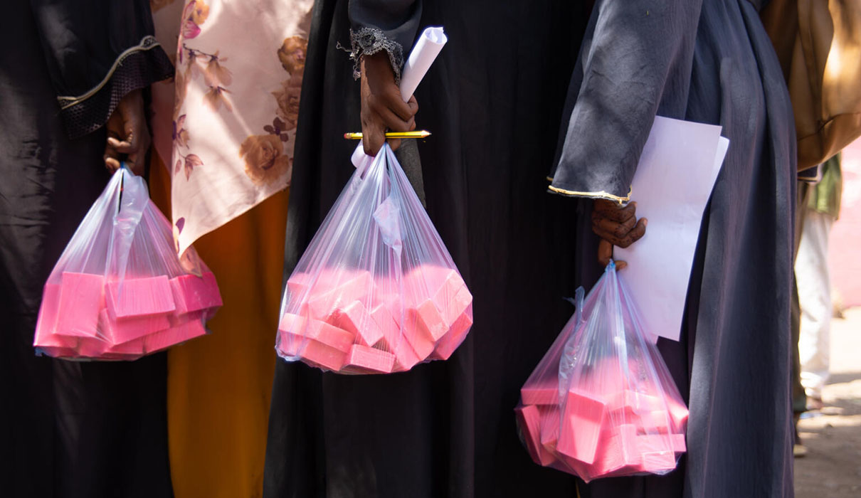 A line of people holding plastic bags of pink soap.