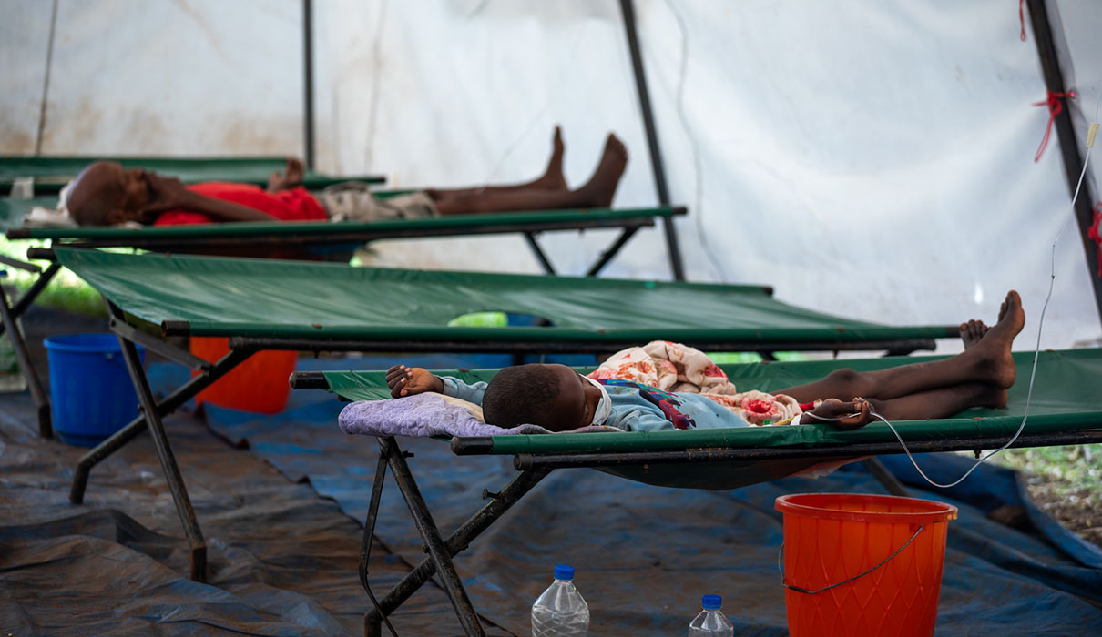 Children lying on green camp beds in a tent.