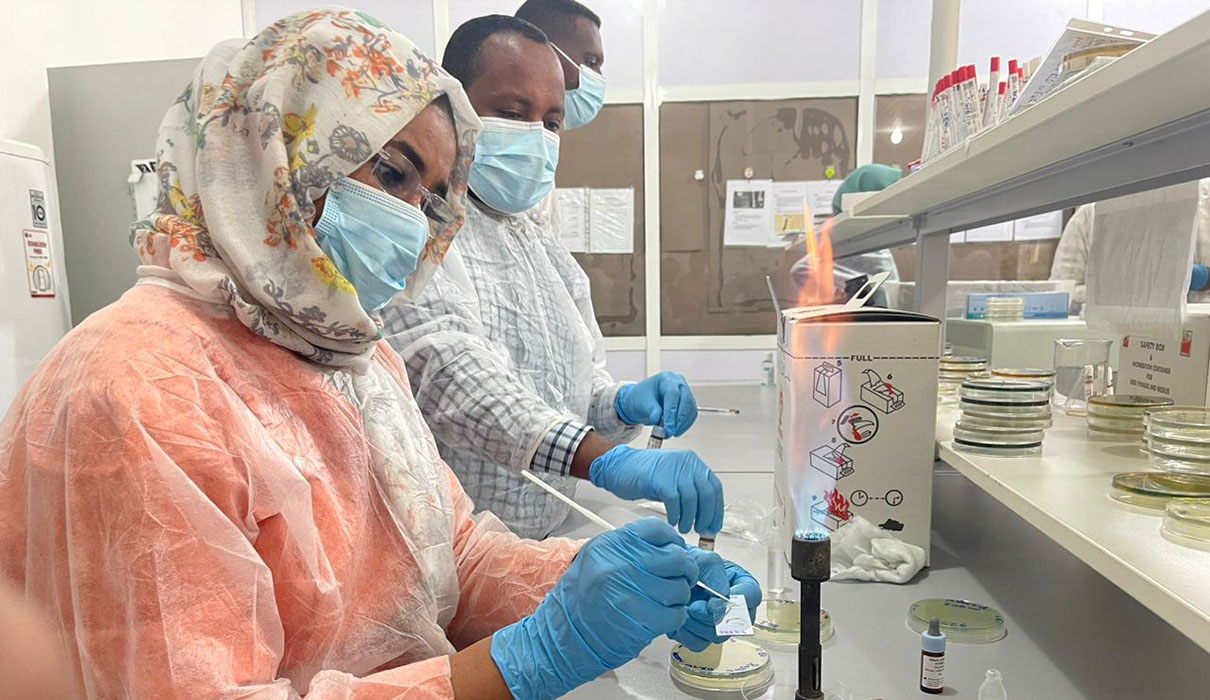 A woman technician wearing protective clothes working with a slide on a work bench.